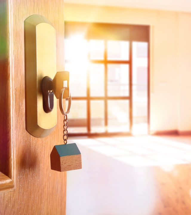 Open entrance door detail of a house with keys in the lock and empty room in the background with golden light effect. Lateral view